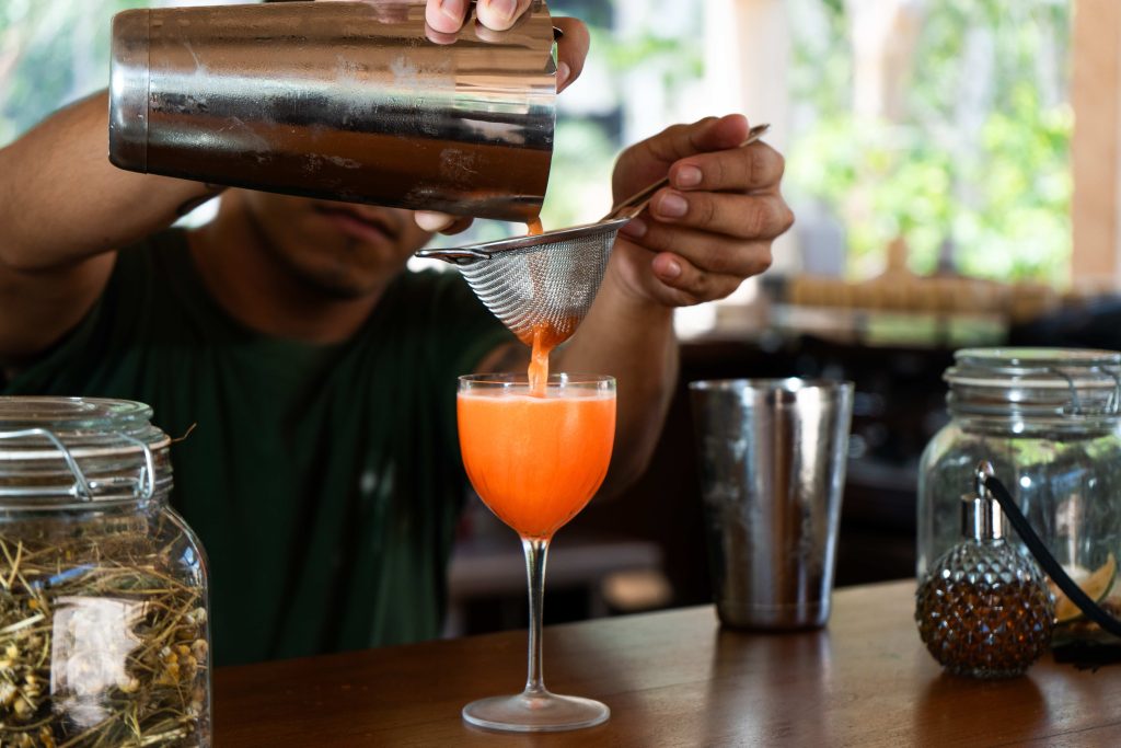 Bartender straining a tropical cocktail into a coupe glass