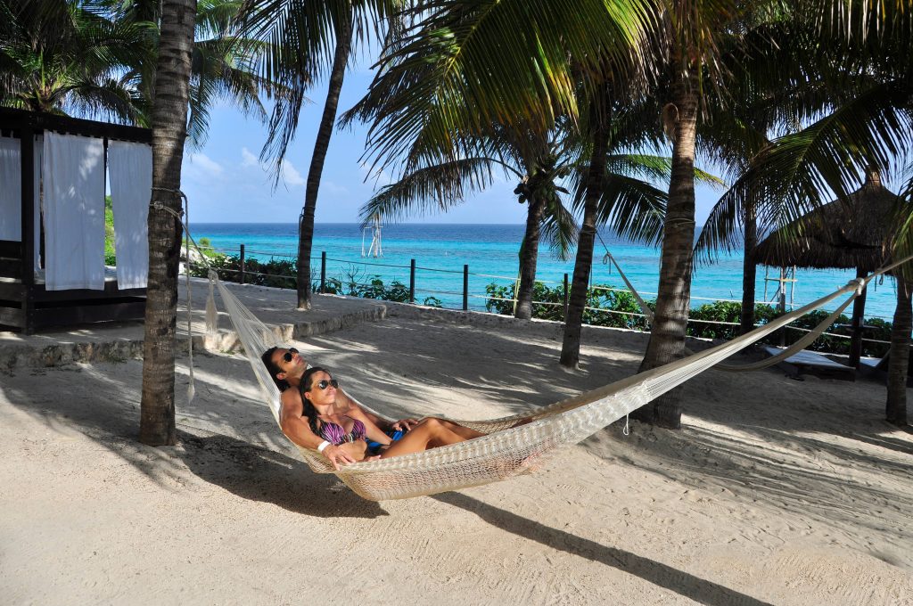 Couple resting in a hammock among palm trees on a beach in Isla Mujeres