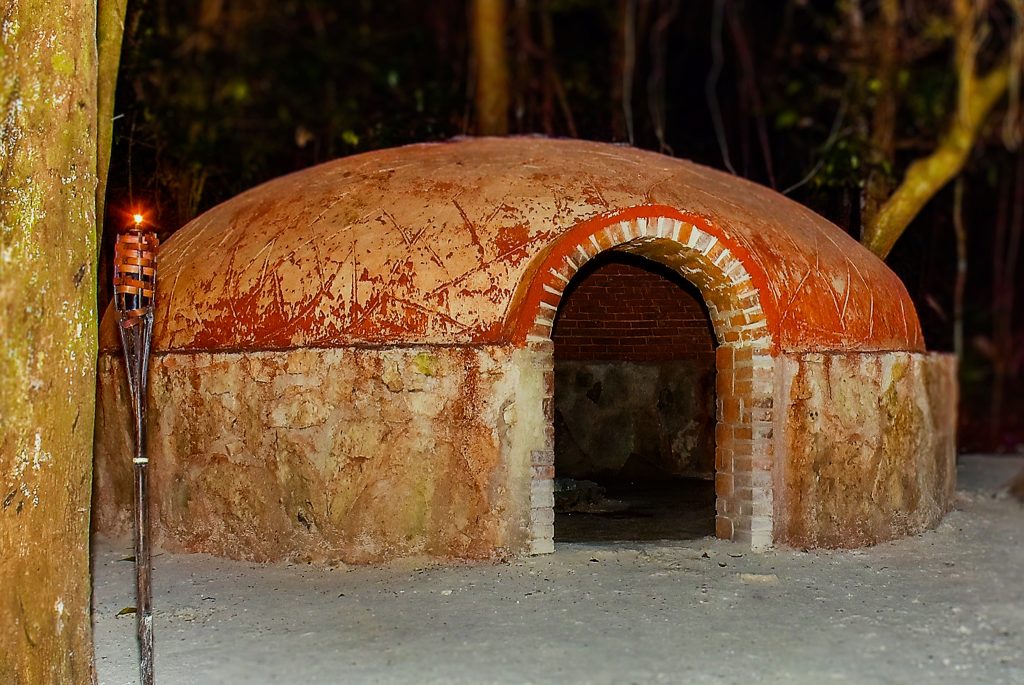 Domed temazcal built of stone and brick, lit by a torch at night