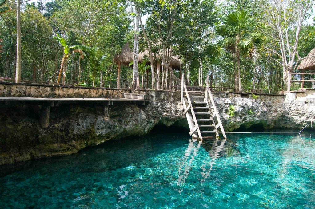 Cenote with a wooden staircase into crystal-clear water near Playa del Carmen