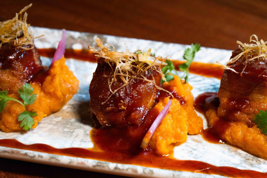Glazed pork bites on a purée, topped with crispy strips and cilantro