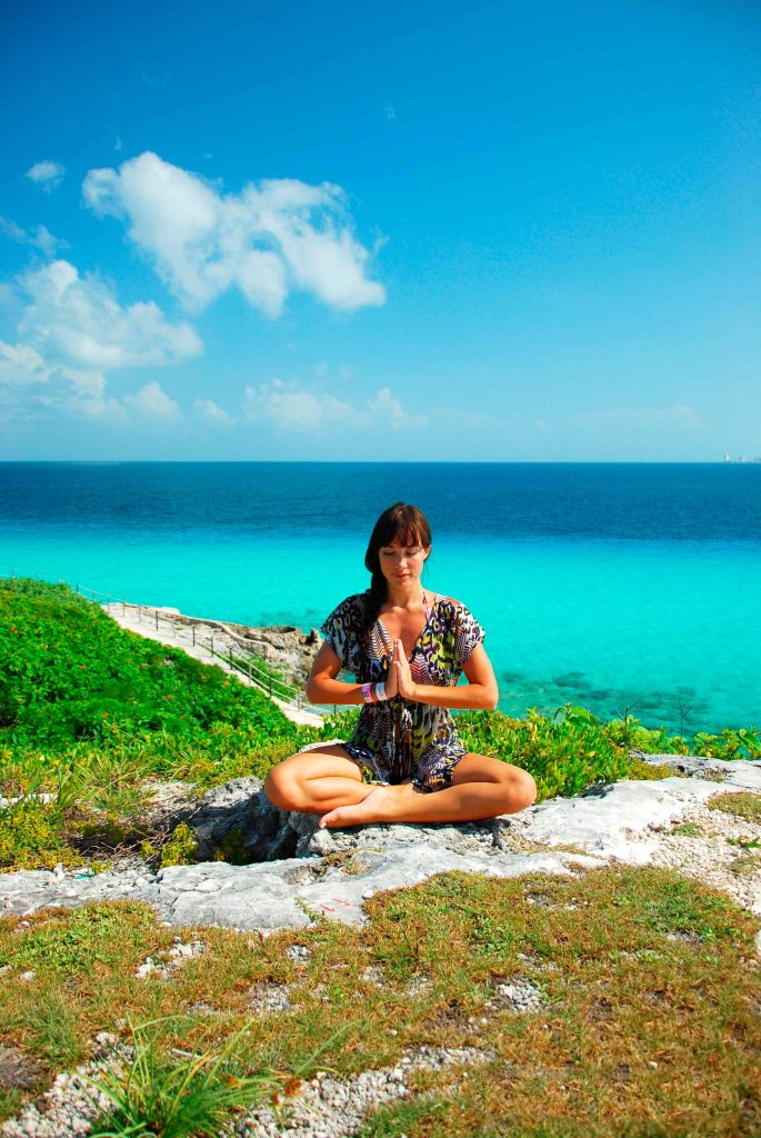Woman meditating cross-legged on a rock above the Caribbean Sea in Isla Mujeres