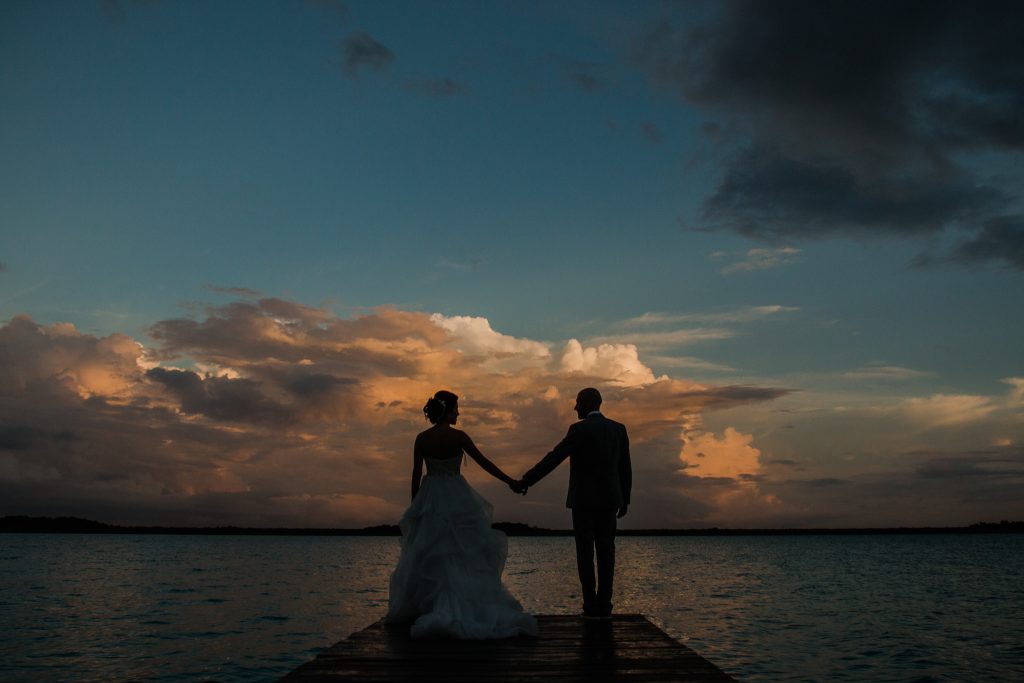 Bride and groom on a wooden dock over the Bacalar lagoon at dusk