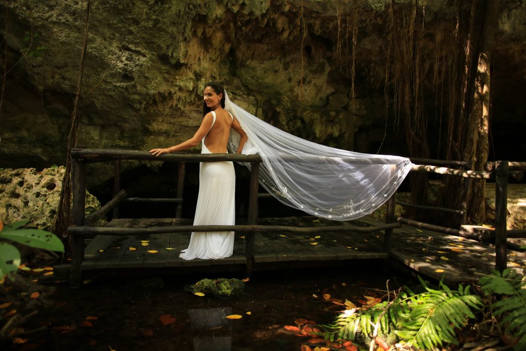 Bride with a long veil on a wooden footbridge at a cenote